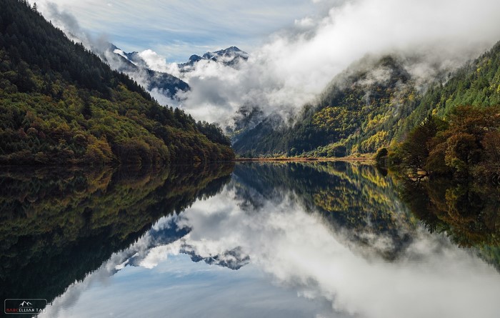 Lake reflecting mountains and clouds in a forest valley