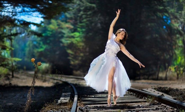 Ballerina in white dress on railroad tracks