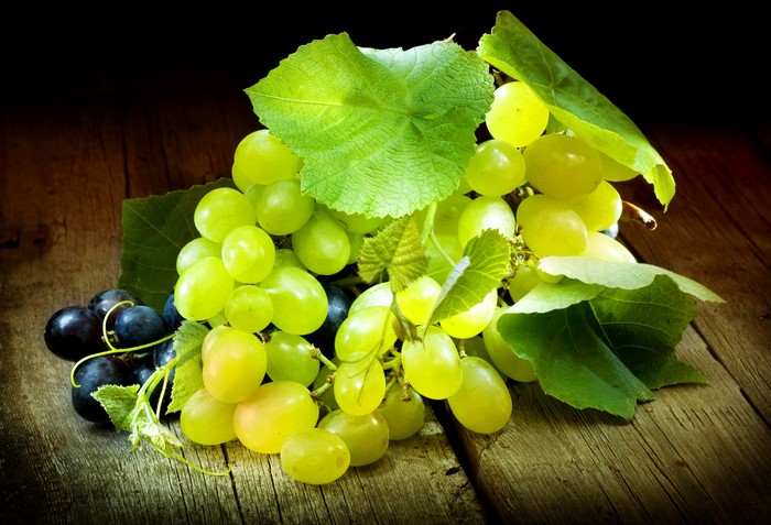 Green and black grapes with leaves on wood