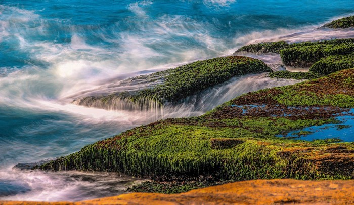 Ocean waves crashing on moss-covered rocks