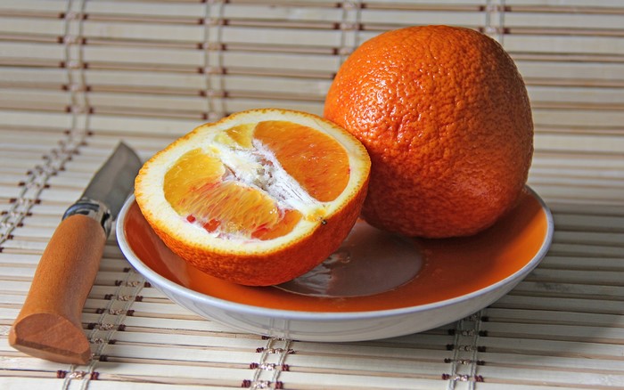 Orange fruit cut in half on a plate with a knife