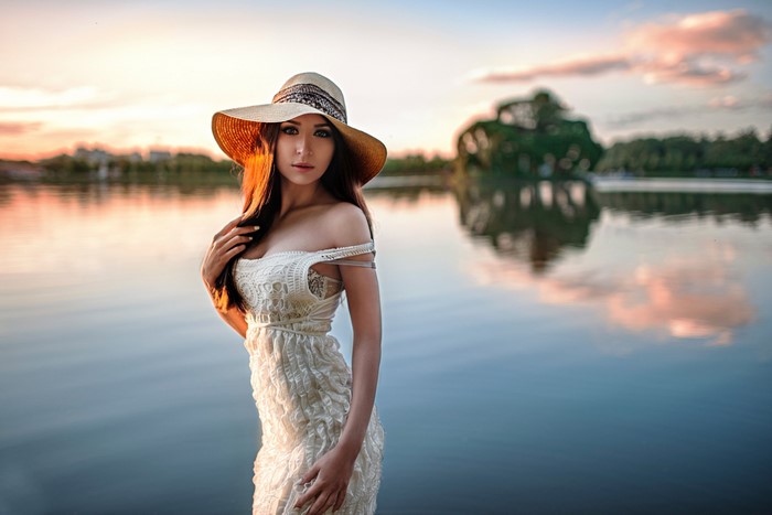 Woman in a hat and dress by a lake at sunset