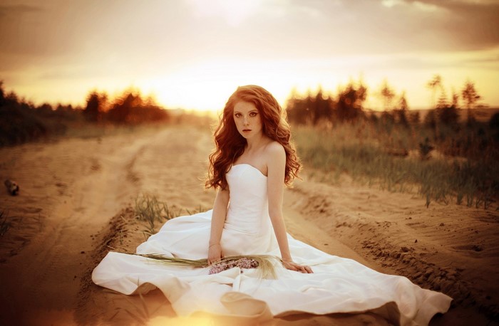 Woman in white dress sitting on sand road at sunset
