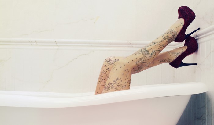 Legs with map pattern tights and stiletto heels in bathtub