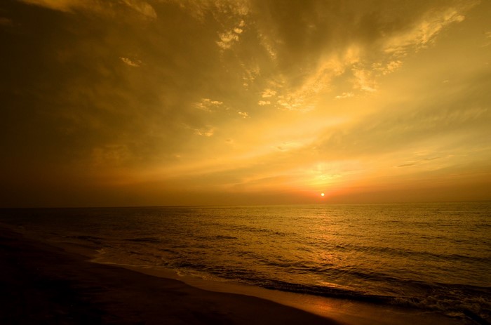 Sunset over the ocean with clouds and beach