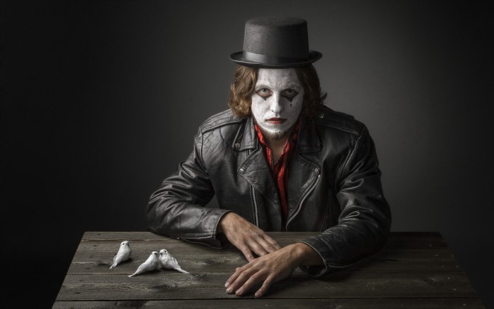 Man with clown makeup and top hat with birds