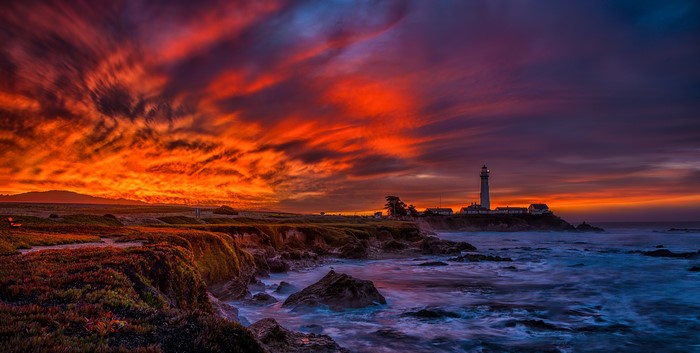 Lighthouse on a rocky coast at sunset with dramatic clouds