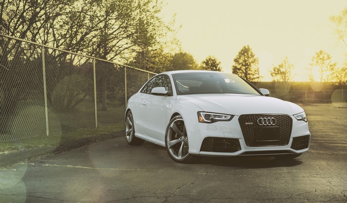 White Audi S5 parked near a fence at sunset