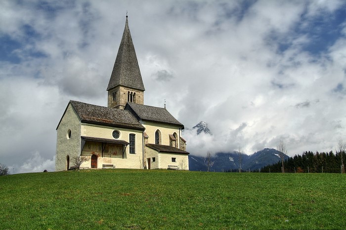 Church with steeple on a grassy hill with mountains in the background
