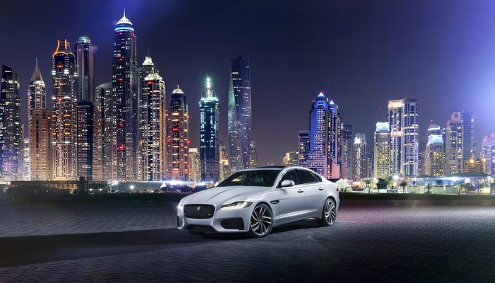 Silver Jaguar XF parked in front of Dubai skyscrapers at night