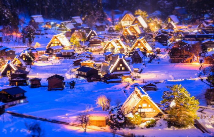 Snowy Japanese village at night with illuminated houses