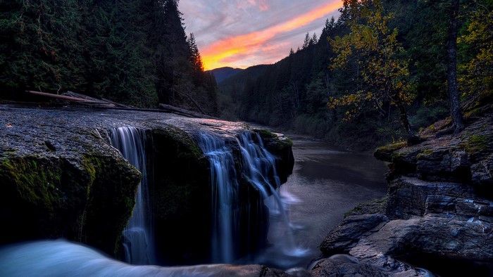 Waterfall cascading over rocks at sunset with forest