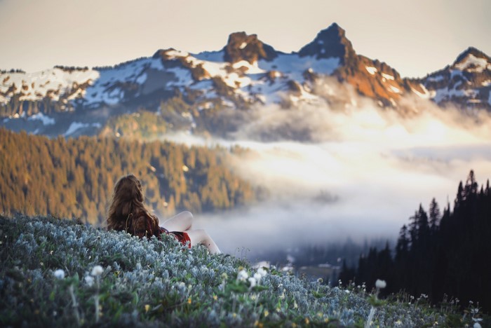 Woman sitting on a mountain overlooking fog and peaks