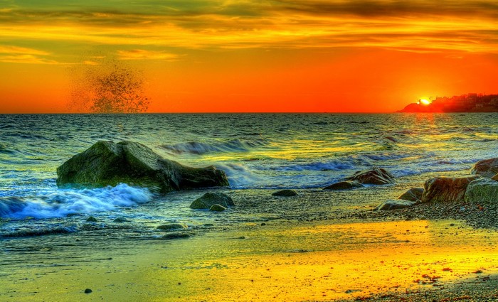 Sunset over the sea with waves crashing on rocks