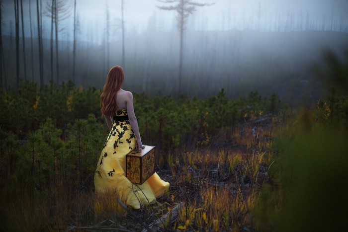 Woman in yellow dress with suitcase in foggy forest