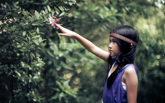 Young girl in Native American costume reaching for flower
