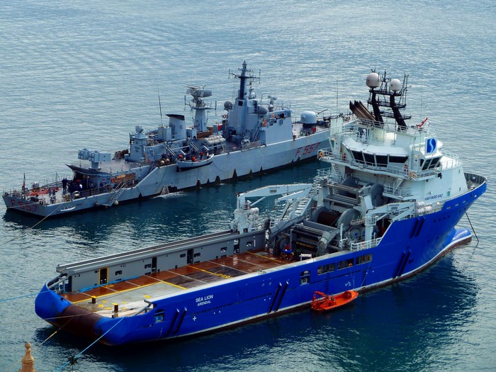 Two ships docked at sea, one blue and one gray