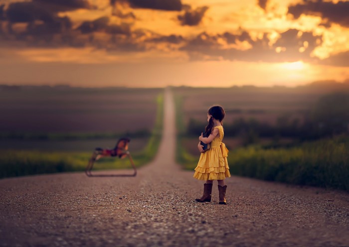 Girl in yellow dress on a road at sunset with toy