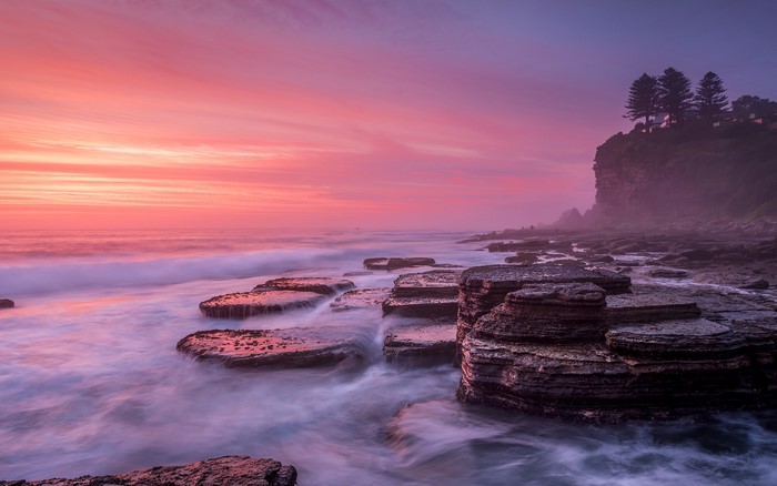 Pink sunset over rocky coastline with ocean waves
