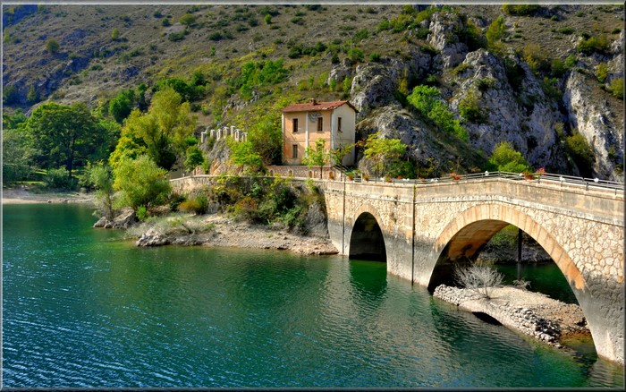 Stone bridge over a lake with a house in Villalago, Italy
