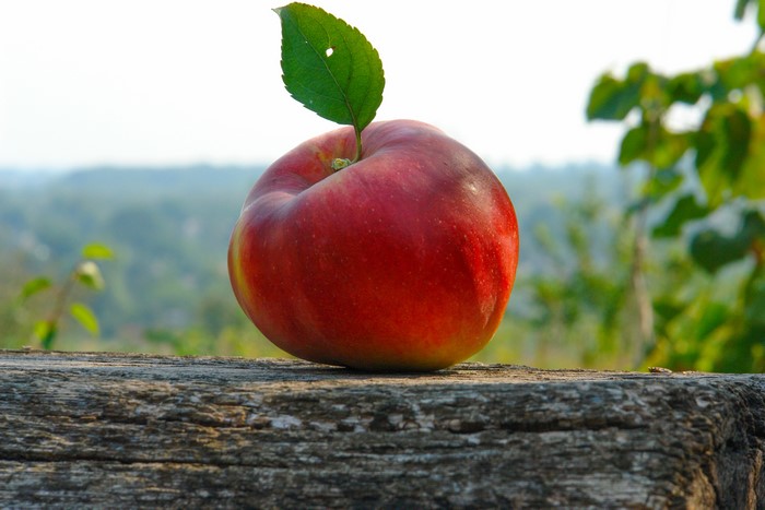 Red apple with a leaf on a wooden surface