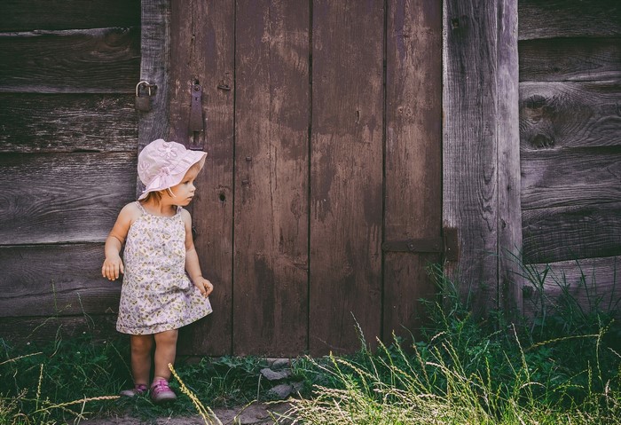 Little girl in a hat by a wooden door