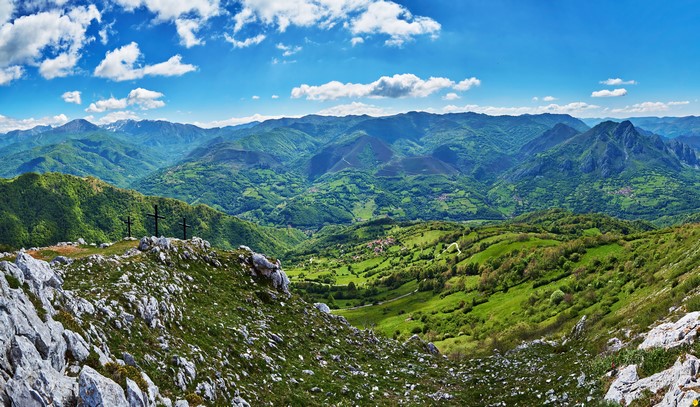 Three crosses on a mountain peak overlooking a green valley in Quiros, Spain