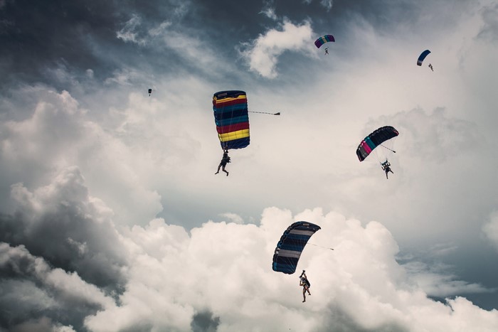 Parachutists descending through cloudy sky
