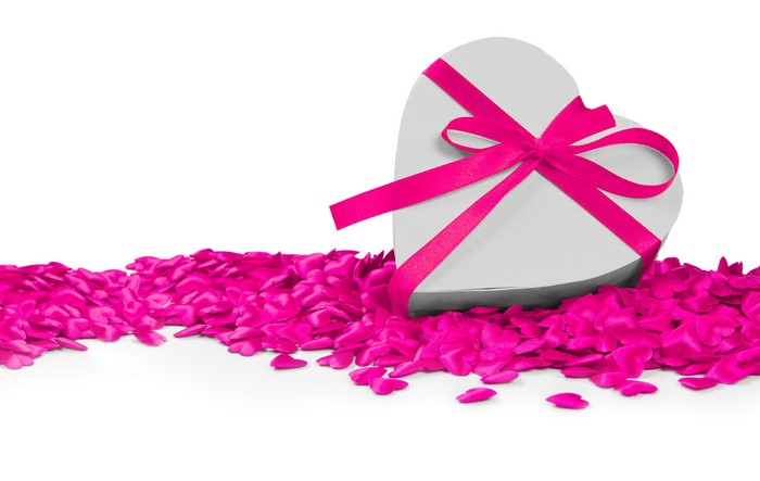 Heart-shaped gift box with pink ribbon on rose petals