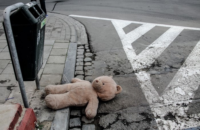 Teddy bear on the street next to a trash can