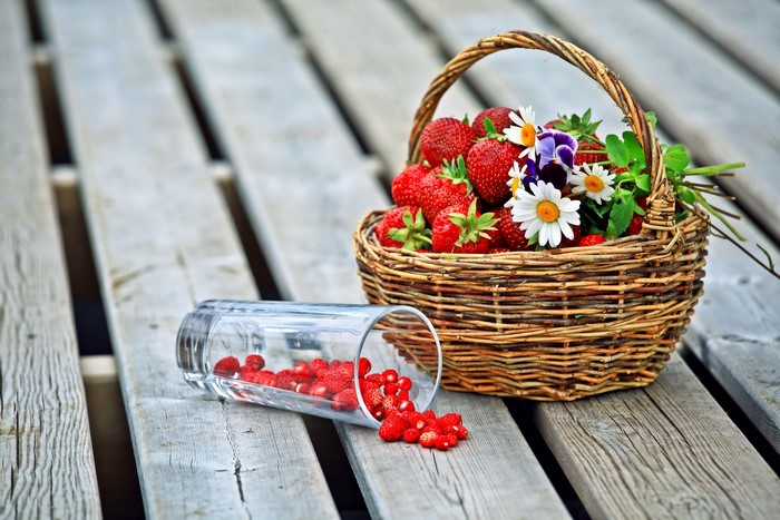 Strawberries in a wicker basket with flowers and spilled glass
