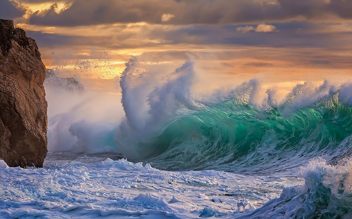 Crashing ocean wave against a rocky cliff at sunset