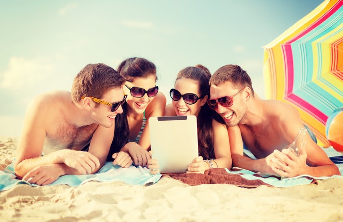 Four friends on a beach looking at a tablet