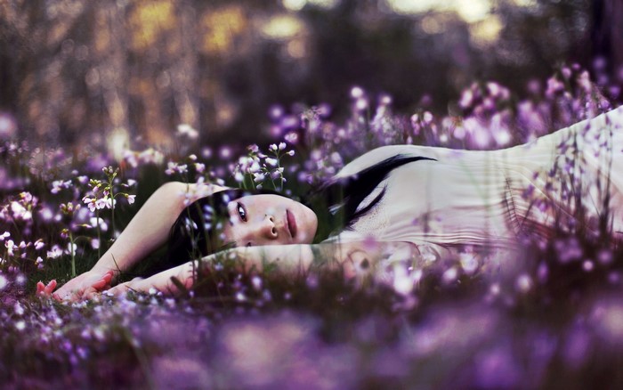 Brunette girl lying in a field of purple flowers