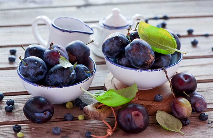 Plums and blueberries in bowls on a wooden table