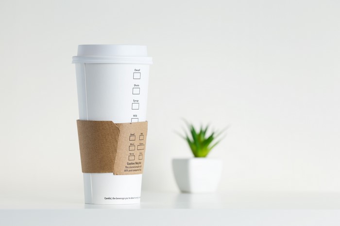 White coffee cup with sleeve and plant