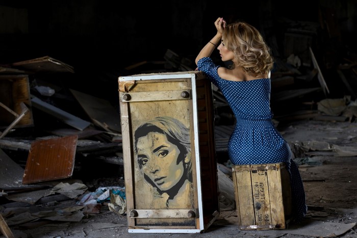 Woman in polka dot dress leaning on a wooden crate with portrait