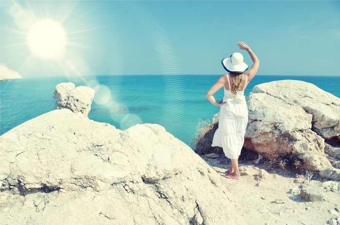 Woman in white dress and hat on rocky coast overlooking the sea