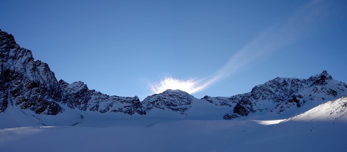 Snowy mountains under a clear blue sky with sun peeking over the peaks