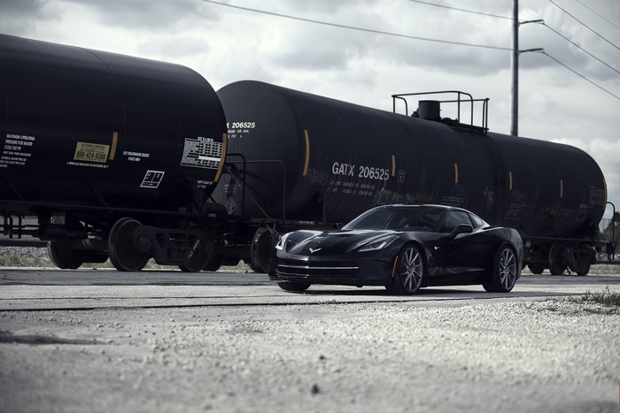 Black C7 Corvette Stingray next to train cars
