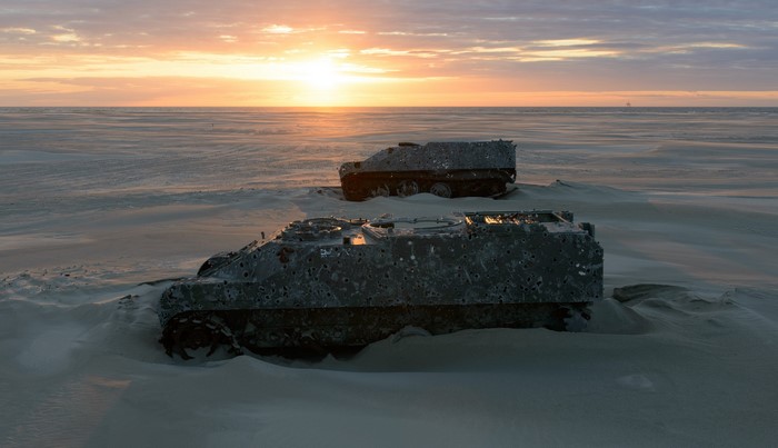 Two military vehicles on a sandy beach at sunset