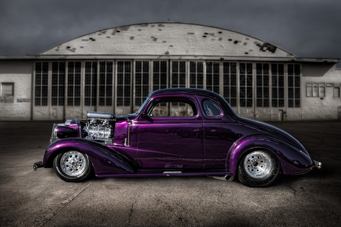 Violet hot rod with exposed engine in front of hangar