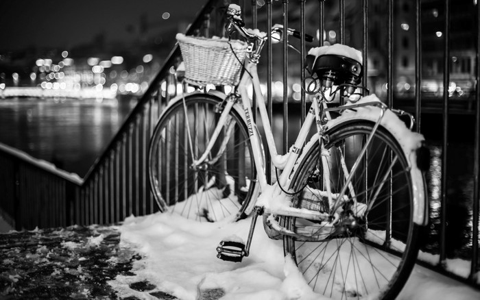 Bicycle covered in snow by a fence at night