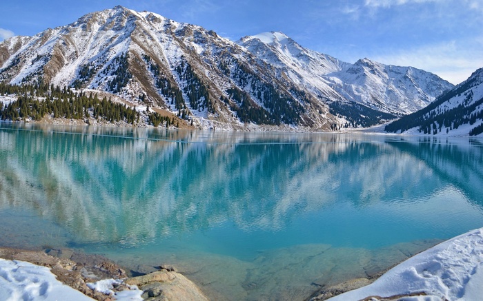 Turquoise mountain lake with snow-capped peaks and pine trees