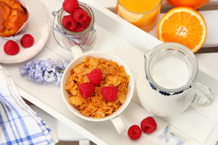 Breakfast tray with cereal, raspberries, muffin, and orange juice