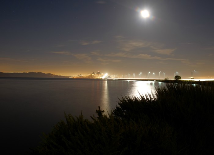 Night view of a bridge over a body of water with the moon in the sky