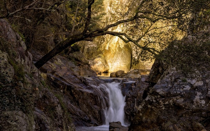 Waterfall flowing over rocks with trees and cliffs