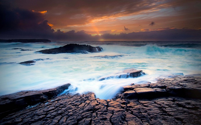 Ocean waves crashing on rocky shore at sunset