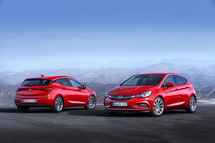 Two red Opel Astra cars on a road with mountains
