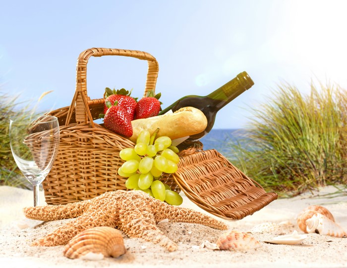 Picnic basket with strawberries, grapes, bread, and wine on the beach